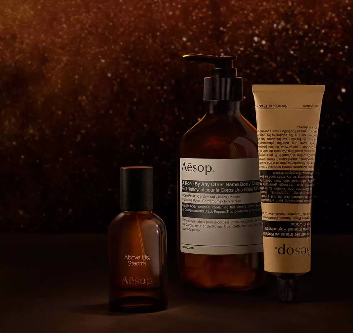 Aesop Above Us, Steorra fragrance bottle, large pump bottle and cosmetic tube arranged on a dark surface.