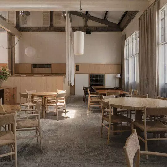 An empty restaurant with high ceilings, timber tables and chairs, and hanging pendant lights.